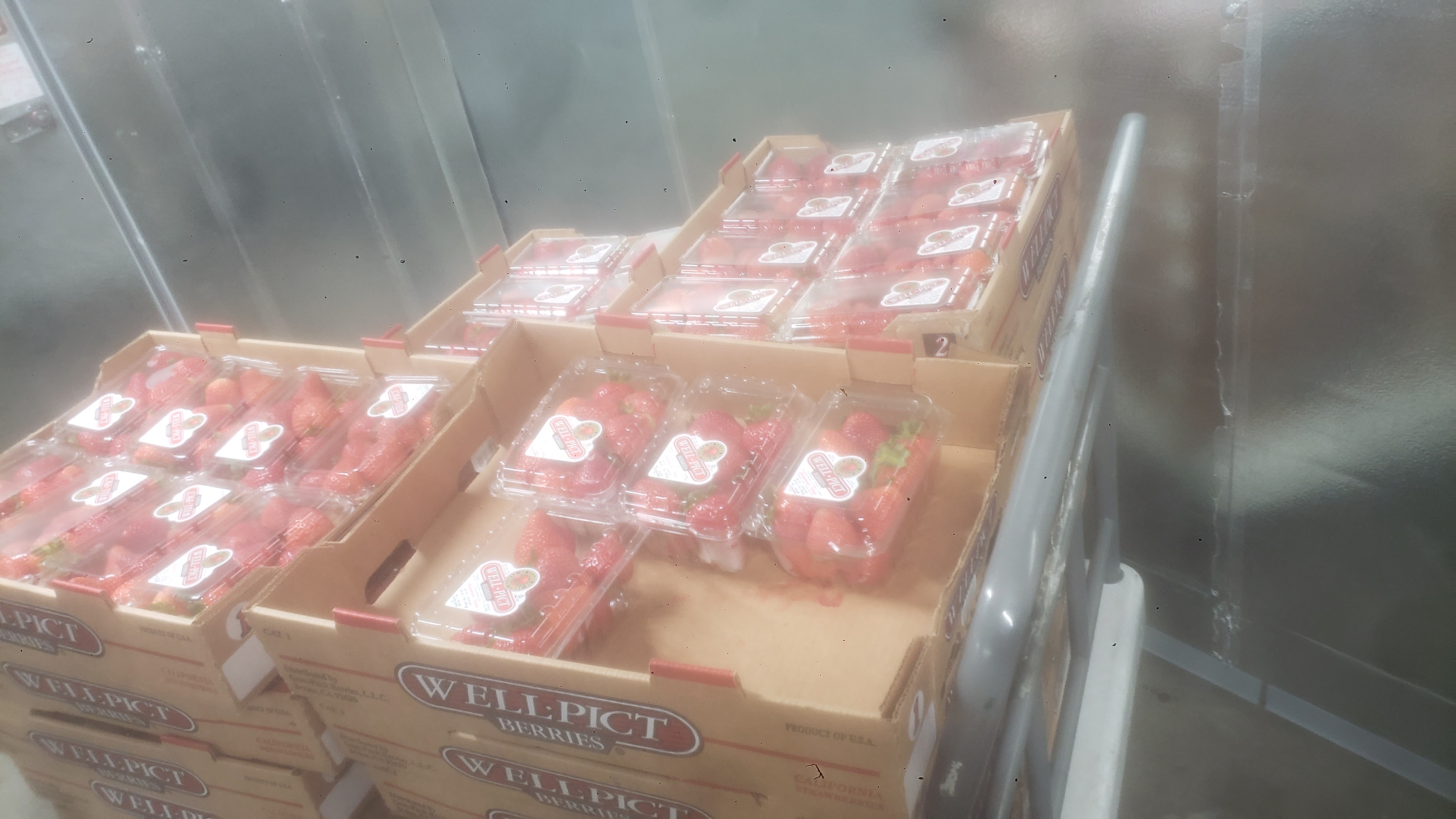Produce trays filled with containers of strawberries on a rolling cart.